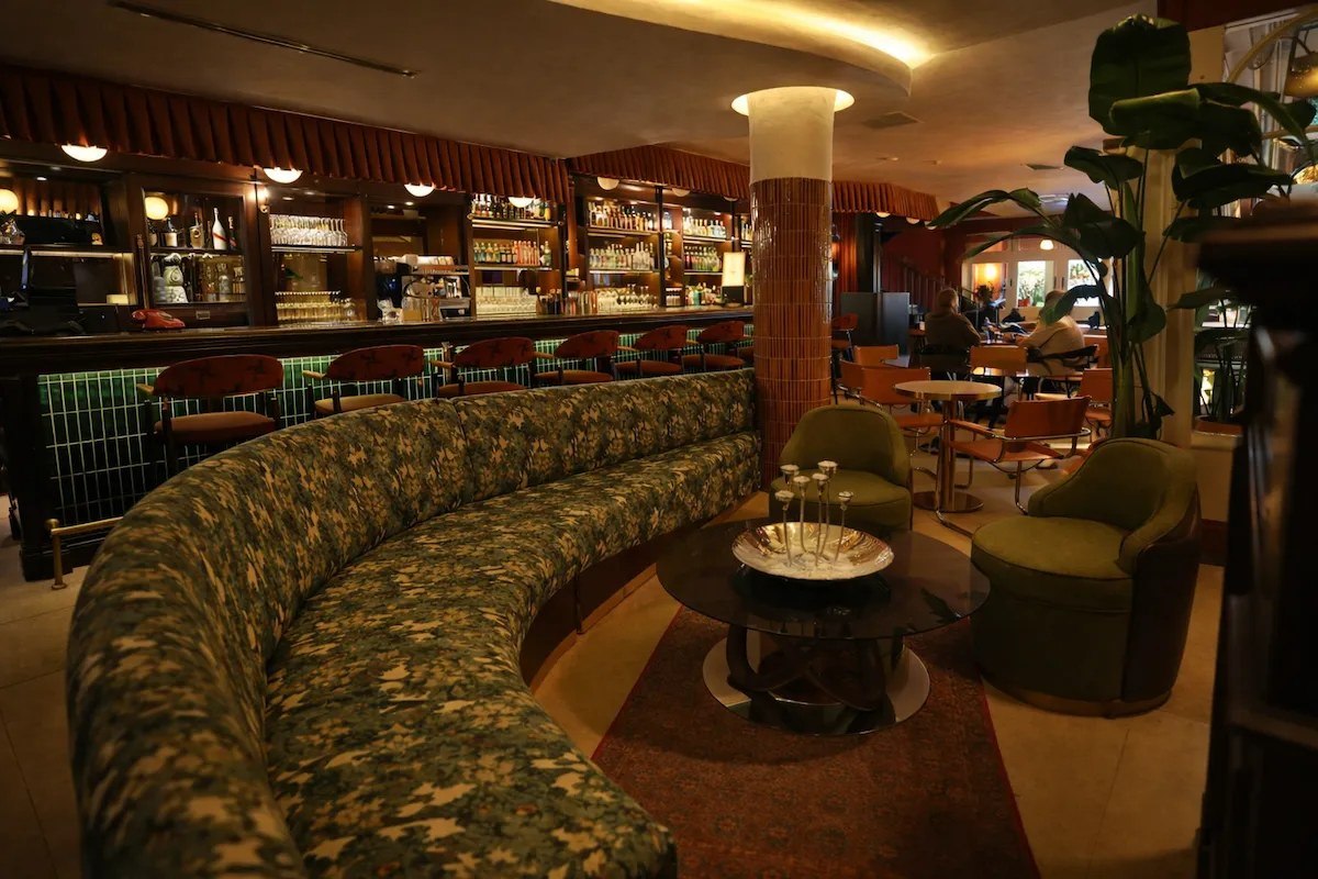 Kadıköy'deki Bias Kitchen'ın sıcak atmosferini yansıtan bu fotoğrafta, alevlerin dans ettiği uzun bar masası önünde kırmızı tonlu sandalyeler, tuğla dokulu duvar ve ışıklandırılmış bir ağaç görülürken, dışarıda gece manzarası seçiliyor.